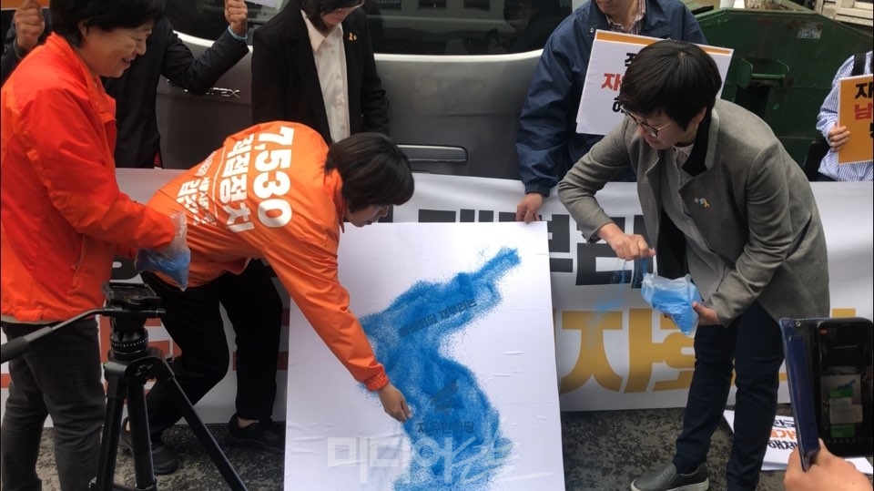 ▲ 24일 민중당이 자유한국당 로고가 쓰여있는 판넬에 모래를 뿌리는 퍼포먼스를 진행하고 있다. 사진=정민경 기자.