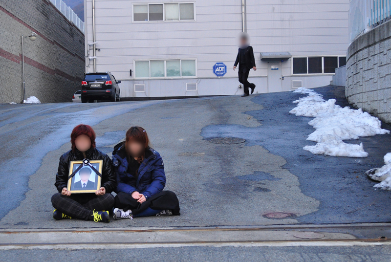 ▲ 2014년 2월 고3 현장실습생 김대환군이 숨진 공장 앞에서 아들의 영정을 들고 앉은 어머니(왼쪽)와 누나. 사진=용석록