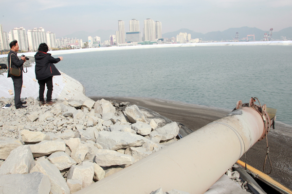 ▲ 2014년 11월11일 매립이 진행되고 있는 마산해양신도시 인공섬. 마산지방해양항만청과 경남 창원시는 마산항 항로 준설과정에서 나온 바다밑 토사를 둥그렇게 만든 인공섬 형태의 호안 안쪽에 투기하는 방식으로 마산만을 매립해 마산해양신도시를 조성하고 있다. 그러나 호안 안쪽에 투기한 준설토 흙탕물이 호안 밖으로 새 나와 마산만을 뿌옇게 만들면서 환경단체가 준설토 투기 중단을 주장하고 있다. 사진속 강철관을 통해 준설토가 호안 안쪽으로 투기된다. ⓒ연합뉴스