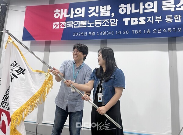 ▲13일 서울 마포구 상암동 TBS 사옥 1층 오픈스튜디오에서 TBS노동조합과 전국언론노동조합 TBS지부의 통합 선포식이 열렸다. 이정환·송지연 언론노조 TBS지부 공동비대위원장이 함께 깃발을 흔들고 있다. 사진=정민경 기자. 
